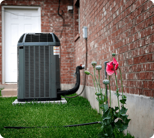 A home air conditioner sitting in the grass next to a flower.