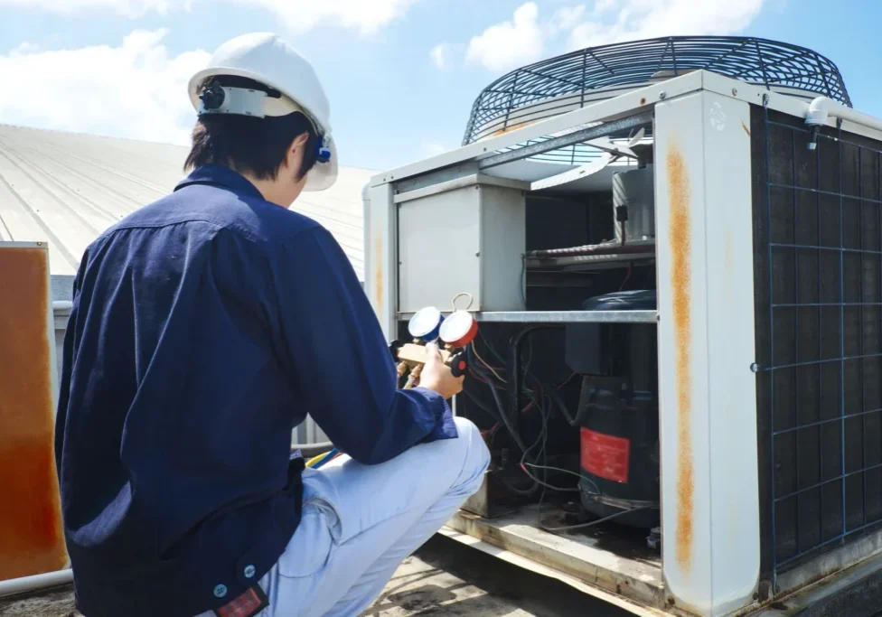 A man in white hard hat looking at an air conditioner.