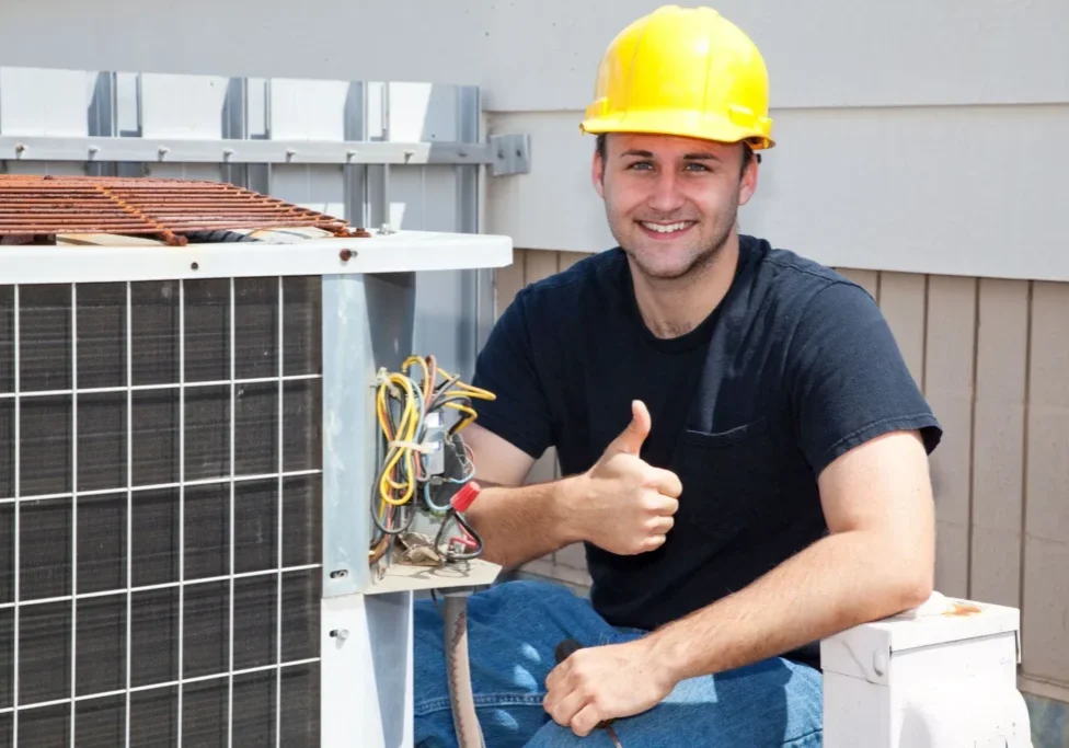 A man in yellow hard hat next to an air conditioner.